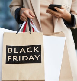 Person holds phone in one hand and bags saying Black Friday in the other