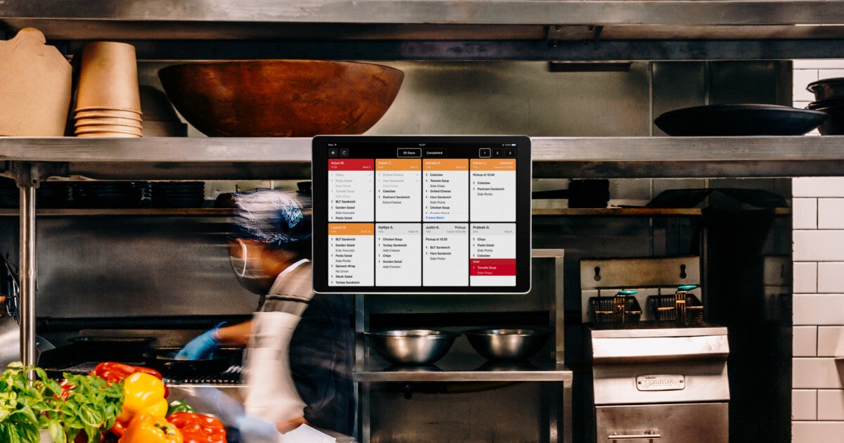 a busy kitchen with a Square KDS system hanging in center frame