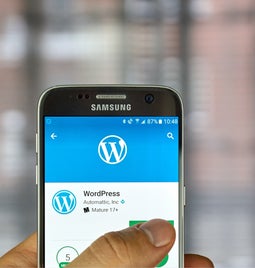 WordPress app shows on a phone with a thumb tapping over it