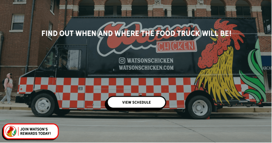 A Watson's Chicken food truck parked in front of a brick building. The truck is white with a red and black logo. The text on the truck says "WATSON'S CHICKEN | Fried Chicken Sandwiches | WATSONSCHICKEN.COM."